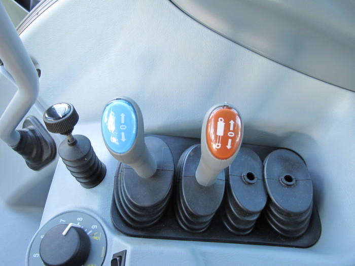 Le débit de la pompe hydraulique s'ajuste en cabine au moyen de la grande molette placée devant les distributeurs.